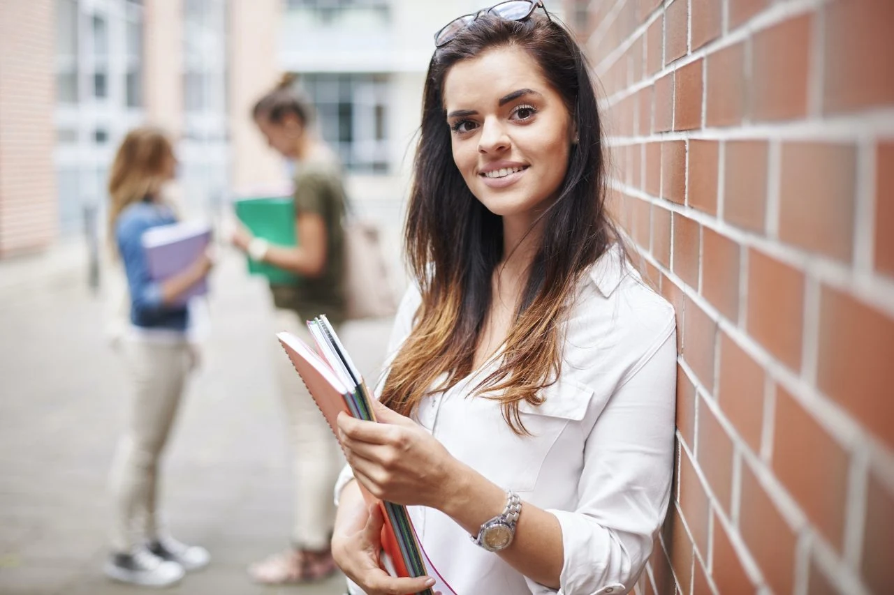NextBrit Student enjoying campus life while holding notebooks outside a university building